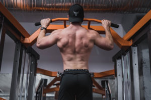 a muscular man performing a wide grip pull up on a horizontal bar at the gym