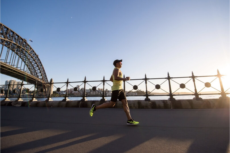 a man with Nike shoes on running next to a bridge and body of water