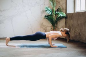 a woman holding a push up position on an exercise mat with a grey wall and green plant in the background