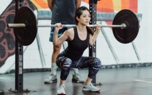 a woman performing a full back squat with a loaded barbell on her back in front of a squat rack