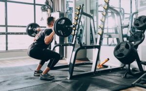 a man performing a back squat with a loaded barbell in front of a squat rack at the gym