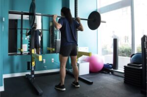 a woman preparing to perform a high bar back squat inside a rack at the gym
