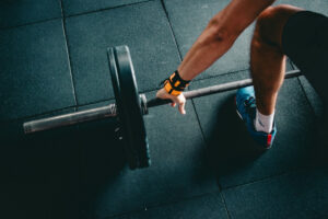 a barbell loaded with two weight plates lying on the gym floor with a person gripping it